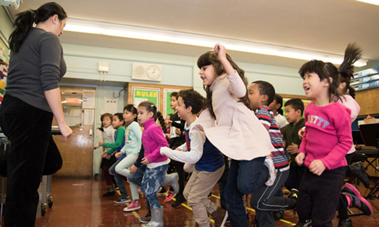 Children follow their teacher's lead, jumping and dancing to a song.