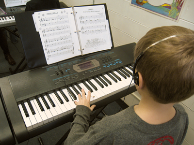 A student carefully places his left hand on the piano as he is reading sheet music.