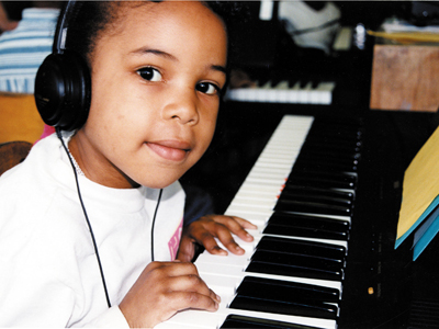 A photo from the early 90s shows a young girl looking at the camera, smiling as she rests her hands on the piano.