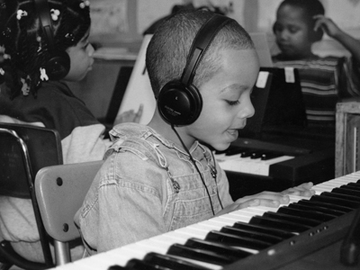 A black and white photo from the early 90s shows a young boy singing to himself while playing the piano.