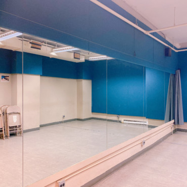 Empty studio with mirrored wall, music stands, fold up chairs, and blocks.
