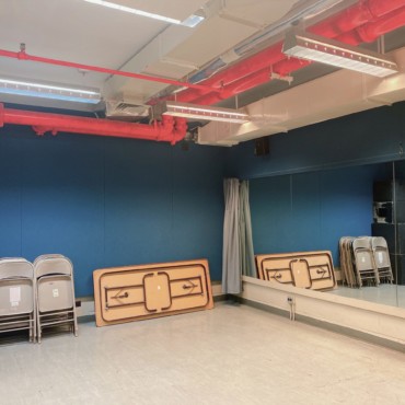 Empty studio with mirrored wall, music stands, fold up chairs, and blocks.