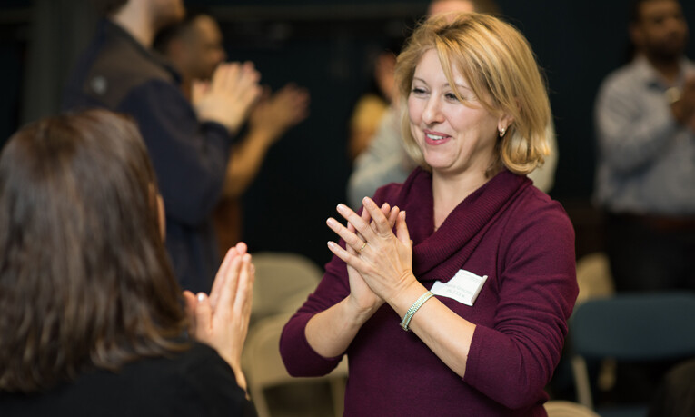 A teacher is at a professional development workshop learning a new game to teach her students. She is smiling and clapping her hands.