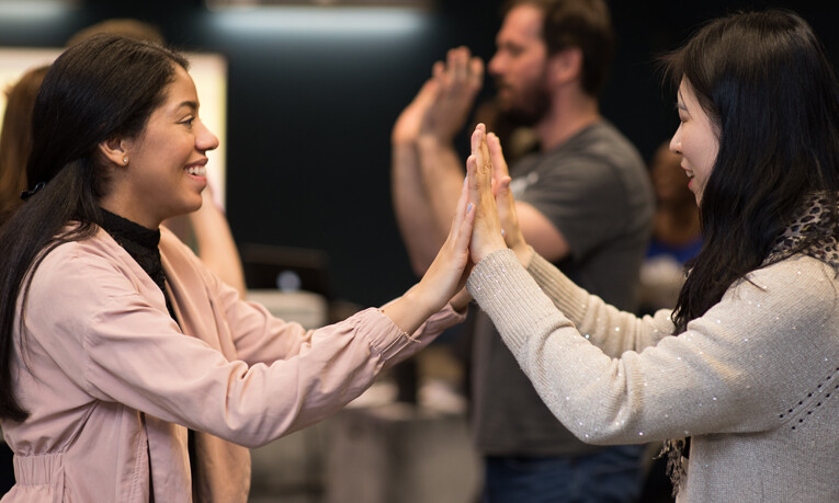 Two music teachers smiling and playing a handclapping game during a professional development workshop.