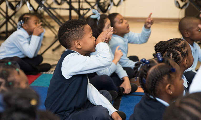 Young children count rhythms. Their hands are pointing and their eyes are focused on the interactive whiteboard.