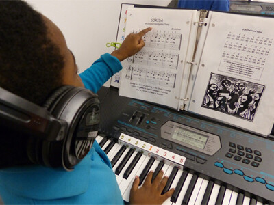 A young student uses his left hand to point at his sheet music while he plays the melody with his right hand.