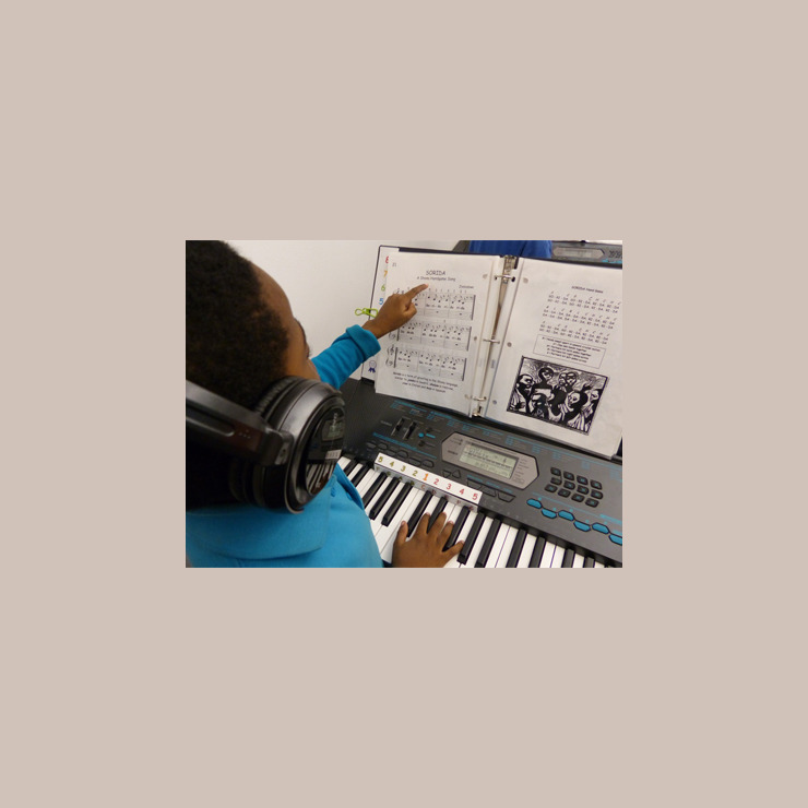 A young student uses his left hand to point at his sheet music while he plays the melody with his right hand.