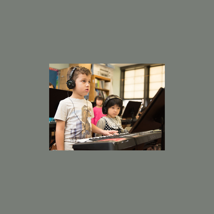 A young boy and a young girl stand together at a piano in class.