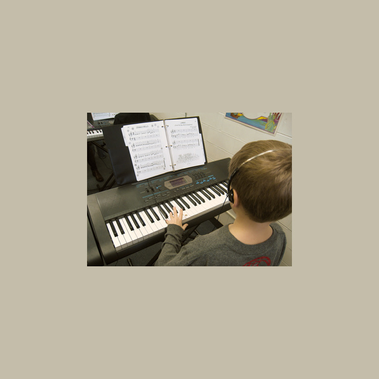 A student carefully places his left hand on the piano as he is reading sheet music.
