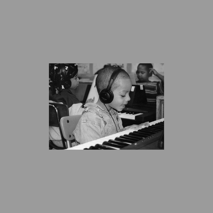 A black and white photo from the early 90s shows a young boy singing to himself while playing the piano.
